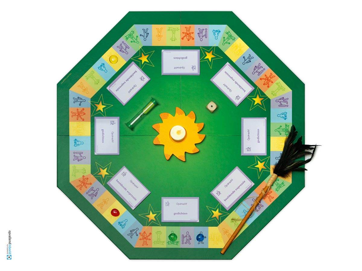Het groene achthoekige spelbord van Ons Bestaan Op Een Bordje staat uitgestald alsof het gespeeld wordt. Een houten dobbelsteen en een groene zandloper liggen erop. Tranen in de vorm van parels liggen op verschillende plekken van het gekleurde achthoekige traject. Een houten zon met een lichtje erin prijkt in het midden van het spelbord. Aan iedere zijde van de acht kanten van het traject ligt een stapel opdrachtkaarten. En een houten praatstok met zwarte veren ligt deels over het traject.