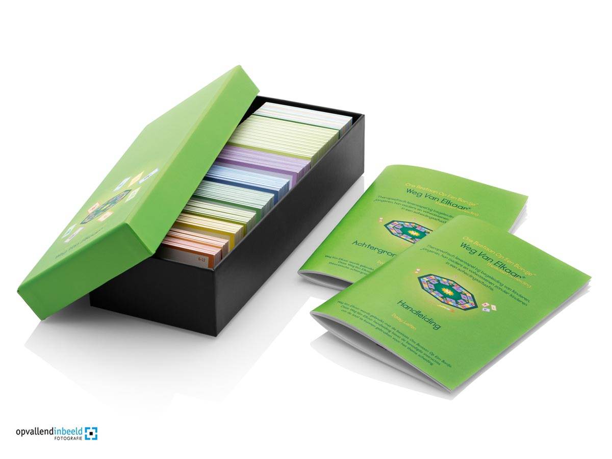 Bij het therapeutische spel Ons Bestaan Op Een Bordje kunnen themasets worden gekozen. Eén lichtgroene kaartenbak met ernaast twee lichtgroene boekjes staan op de foto. De themaset Weg Van Elkaar (na scheiding).
