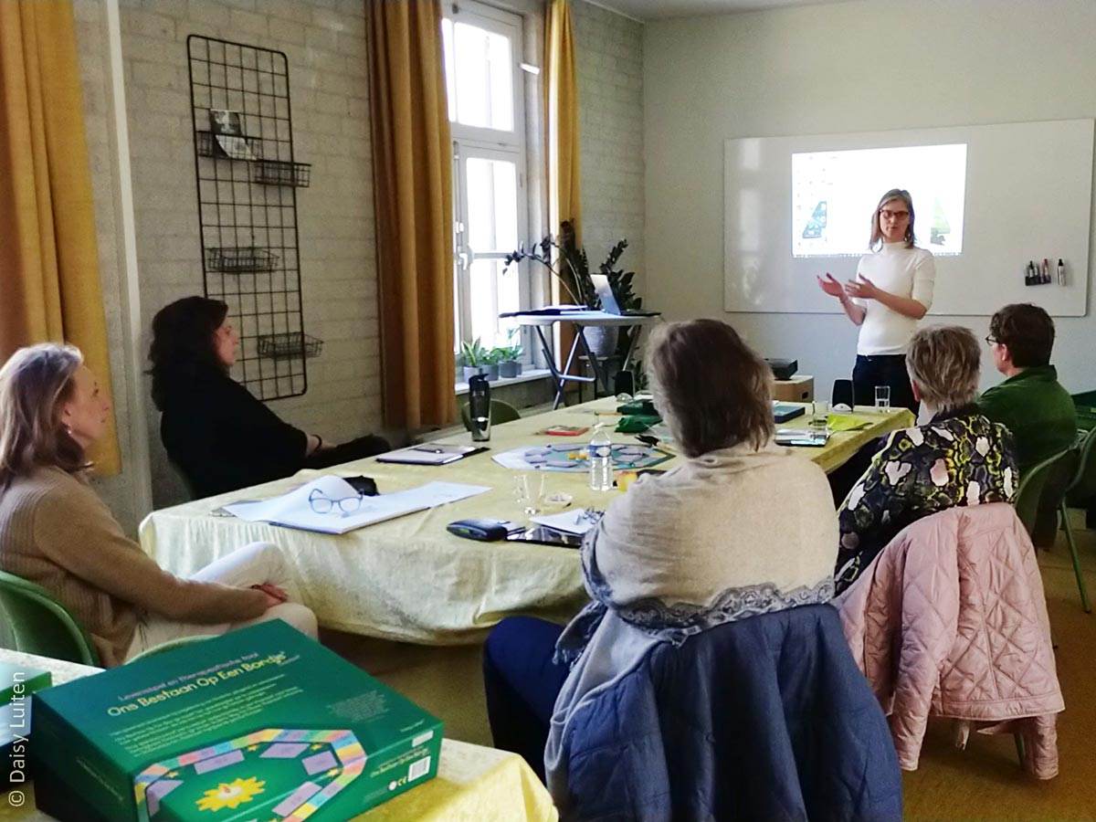 Daisy Luiten staat voor een groep van vijf mensen aan een tafel. Ze geeft een presentatie, achter haar prijkt een scherm. Leer Ons Bestaan Op Een Bordje te gebruiken met je cliënten. Inspirerende training die door deelnemers als zeer waardevol wordt ervaren.